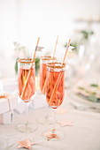 Three gold-rimmed glasses of pink sparkling wine with straws