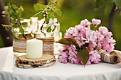 Candle on wooden coaster, cherry blossom and peonies on garden table