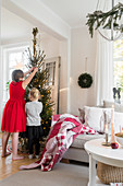 Girls decorating Christmas tree next to sofa in living room