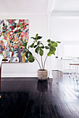 Large houseplant in addition to art value in an open living room with dark wooden floorboards