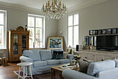 Pale loose-covered sofa, glass-fronted cabinet and chandelier in living room
