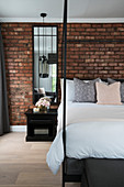 Black four-poster bed in front of exposed brick wall