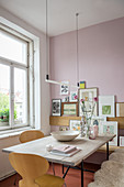 Hängeleuchte über Esstisch mit Holzplatte, im Hintergrund Bildergalerie an rosa Wand