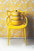 Gelber Designerstuhl mit Kochtöpfen vor gelb-weißer Tapete
