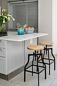 Vase of lilies, kitchen utensils and fruit bowl on island counter with barstools