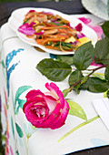 A pink rose and sautéed chicken with peperoni and rose petals on a garden table