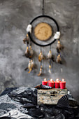 Rote Kerzen auf alter Holzkiste mit mystischer Ethno-Deko in Grau