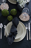 Gedeckter Tisch mit dunkler Tischwäsche, beigefarbenem Geschirr und DIY-Mooskugeln