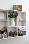 Vase of leaves, toy figurines and basket of folded cloths on white shelves