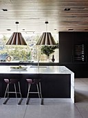 Elegant kitchen island with marble worktop, bar stool and hanging lamps in an open living room