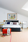 Doppelbett mit Designerstuhl als Nachttisch und roter Polsterhocker auf gemustertem Teppich im Schlafzimmer