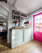 Decorative signs with various mottoes above sideboard next to hot-pink lattice door