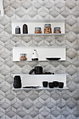 Storage jars, crockery and vases on wall-mounted shelves on monochrome patterned wallpaper