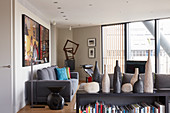 Vases on top of bookcase in front of lounge with grey upholstered furniture