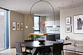 Designer lamp above dining table and chairs in open-plan interior with fitted kitchen in background