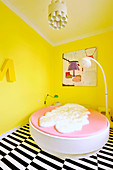 Round bed and standard lamp in bedroom with yellow walls and lack-and-white striped carpet