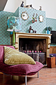 Velvet easy chair with large cushion in front of old fireplace and patterned wallpaper