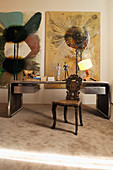 Desk with metal frame, antique carved wooden chair and modern artworks on wall