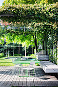 Green table with chairs, bench and grill on wooden terrace, trampoline in background