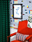 Red armchair in front of designer wallpaper and drawing in black frame