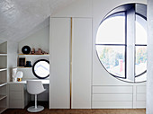 Table and chair next to elegant built-in wardrobe, view through porthole into the open