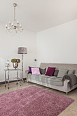 Scatter cushions on grey sofa, silver standard lamp and serving trolley, dusky-pink rug and chandelier in living room