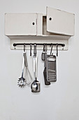 Wall-mounted cabinet with kitchen utensils hung from hook rail below