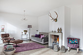 Lilac easy chair next to fireplace, grey sofa, standard lamp, serving trolley and classic chair in living room