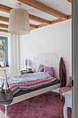 White metal bed in bright bedroom with wooden ceiling beams