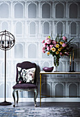 Upholstered chair and console table against wallpaper with architectural motif
