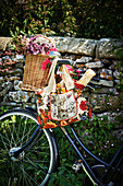 Weidenkorb mit Blumen und blumige Einkaufstasche mit Baguette am Fahrrad