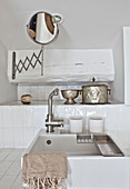 Sink, silver pots and shaving mirror in bathroom with white wall tiles