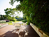 Weißer Tisch und Stühle auf Holzterrasse, seitlich Bambuspflanze als Sichtschutz