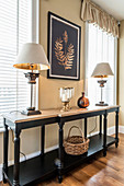 Two table lamps on black console table in front of two windows