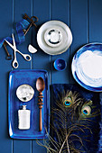 Schalen, Kissen mit Pfaufedern und Tablett mit Holzlöffel und Flakon auf blauem Tisch