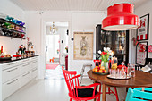 Round table and chairs below red lampshade in white kitchen-dining room
