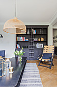 Metal coffee table, dark bookcase with library ladder and chairs in living room with herringbone parquet floor