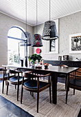 Dark dining table with chairs, hanging lamps from old fishing baskets in the room with a white-painted brick wall