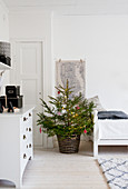 Geschmückter Weihnachtbaum und weiße Kommode in weißem Zimmer