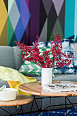 Vase mit Blätterzweig auf Coffeetable, im Hintergrund Sofa vor bunter Tapete