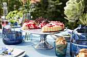 Outdoor table setting with fruit tart, flowers and artichokes in glass vases