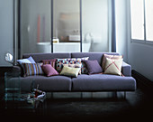 Cushions on lilac sofa in front of glass sliding door leading into bathroom