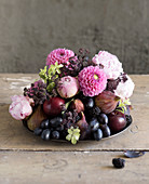 Spätsommerliches Gesteck aus Obst und Blumen in Rosa bis Violett