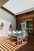 Dining table on terrace with sunlight falling through slatted roof