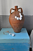 Bead necklace around clay amphora on light blue wooden box