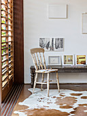 Collection of pictures on rustic wooden bench and wooden chair on cowhide rug next to window with louvre blinds