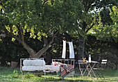Metallbett und Gartenmöbel unterm Baum im mediterranen Garten