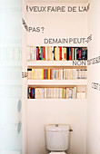 Toilette mit Bücherregal und Sprüchen aus schwarzen Reißnägeln an der Wand