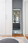 View through doorway flanked by wardrobes into bathroom with grey washstand against ornate wall tiles
