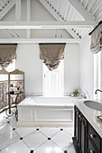 Vintage-style bathtub and washstand, exposed wooden roof structure and marble floor tiles in white bathroom